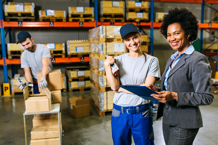 Black female materials handling professional and white female warehouse employee, with male employee in background